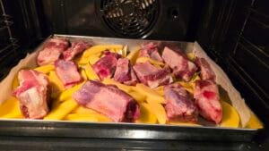 Costine e patate disposte in teglia pronte per la cottura
